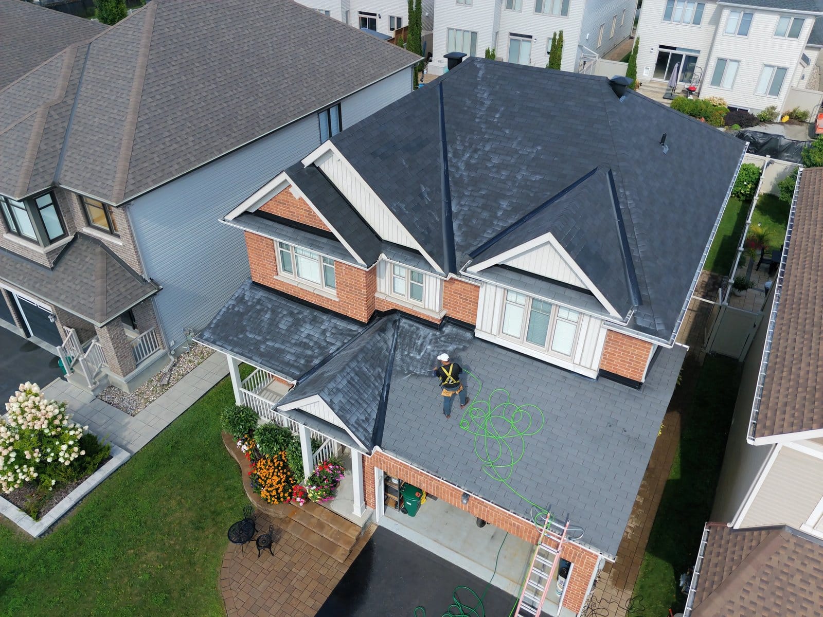 Aerial view of a technician applying roof rejuvenation treatment along a residential roof.